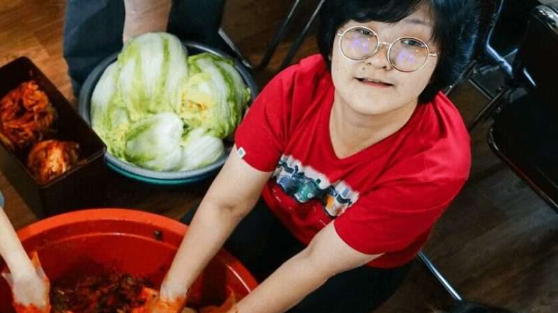 Two people mixing kimchi together in a large bowl